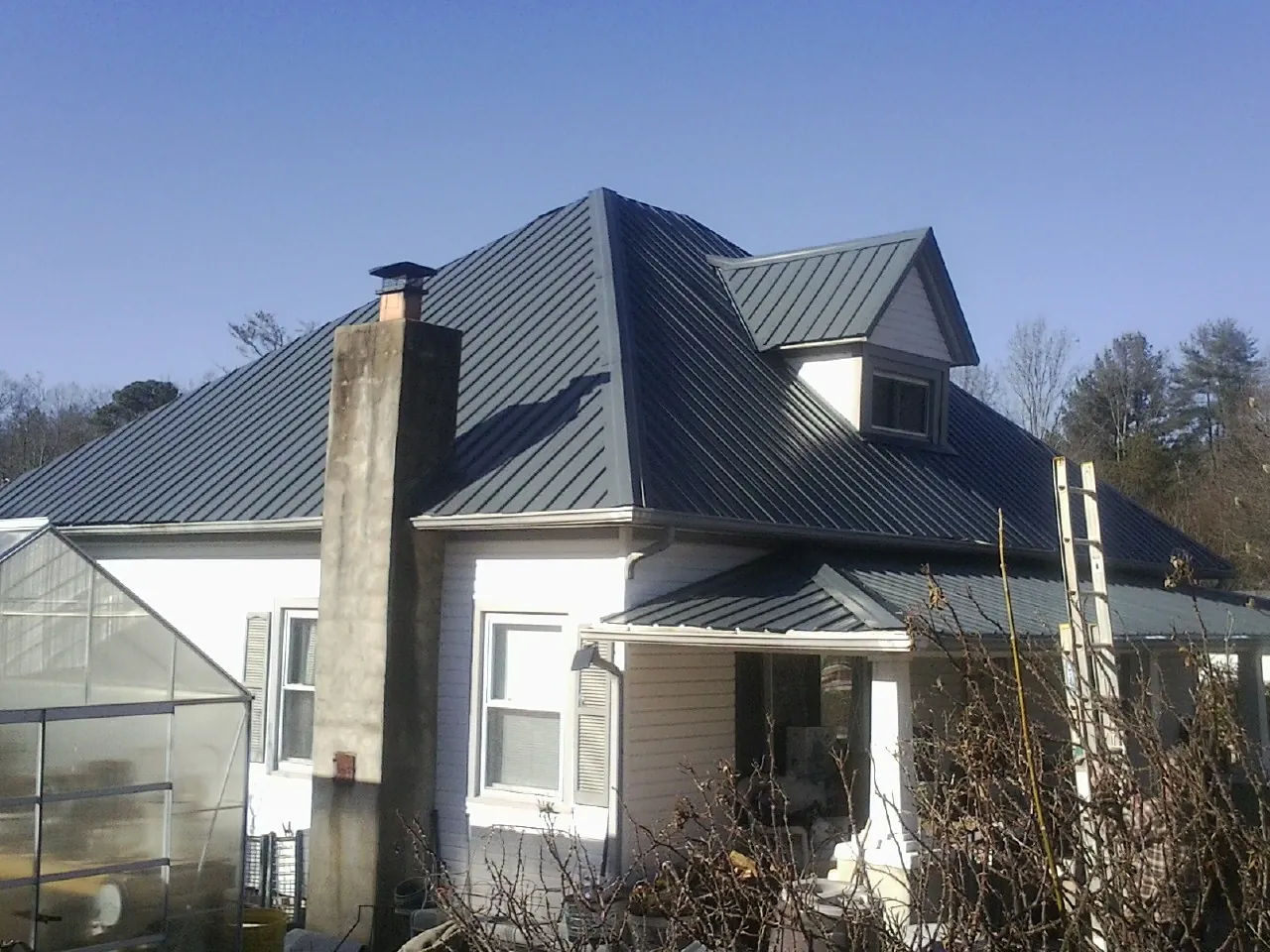Dark blue standing seam metal roof on a white farmhouse with dormer — Slate & Tile Roof Repair by Roofing Brothers in Wilson Creek