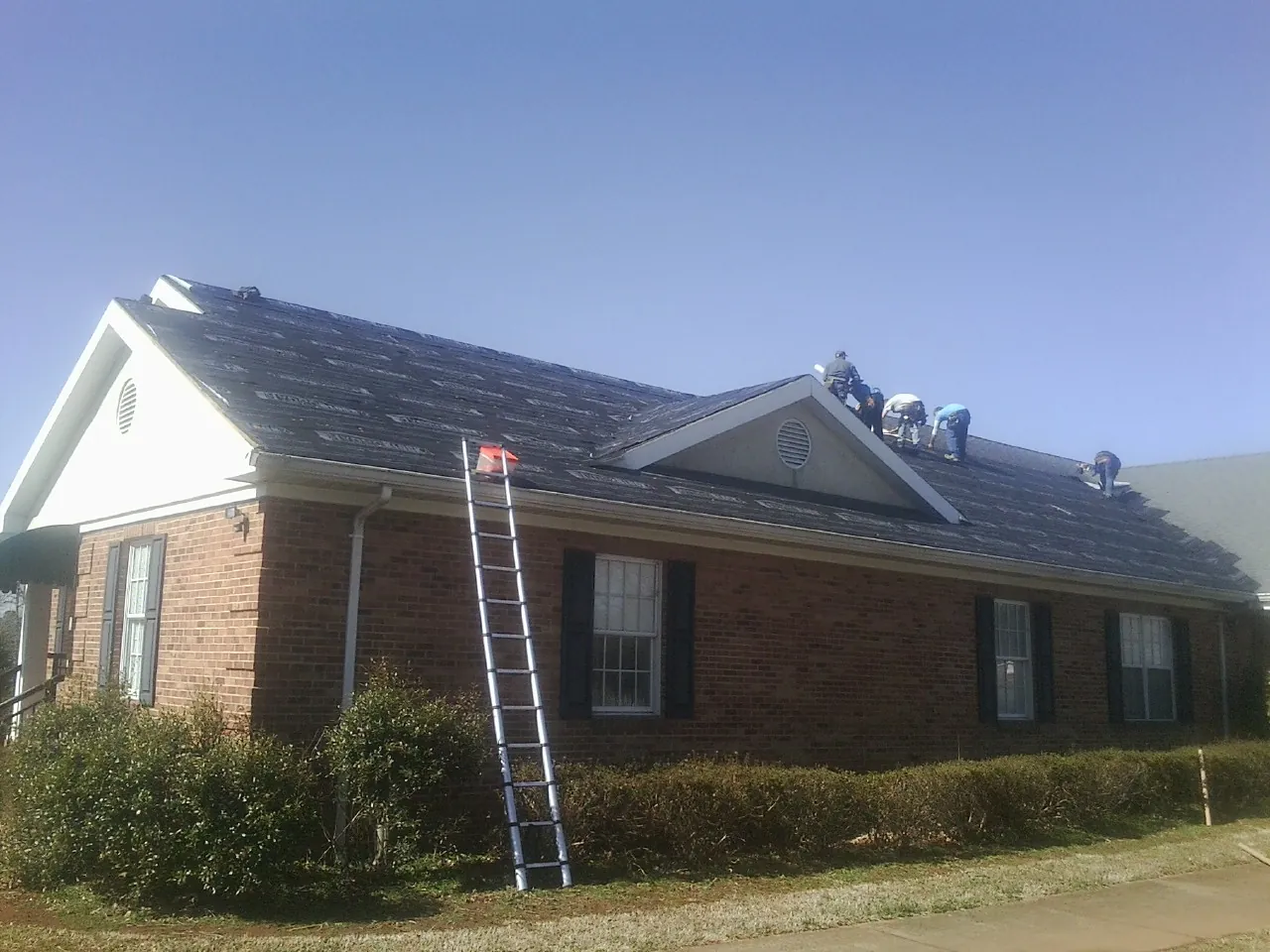 Crew tearing shingles off a brick ranch roof with a ladder set — Metal Roof Repair work by our crew in Wilson Creek