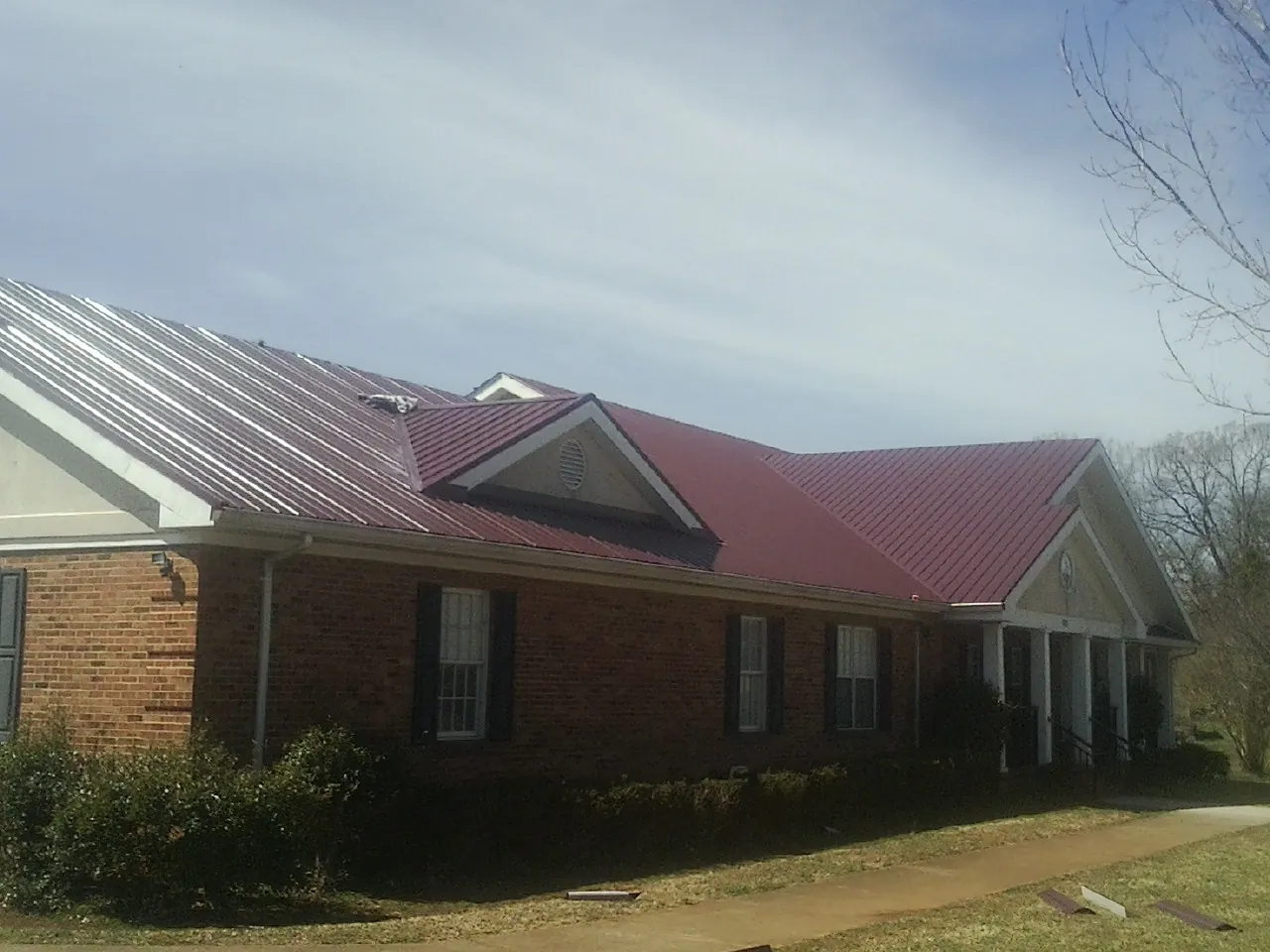 Red metal roof with gabled entries on a long brick building, from a Hail Damage Roof Repair job in Wilson Creek