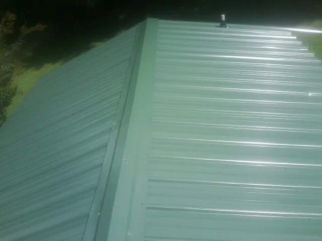 New green metal panels meeting at the ridge of a roof — Flat Roof Repair work by our crew in Wilson Creek
