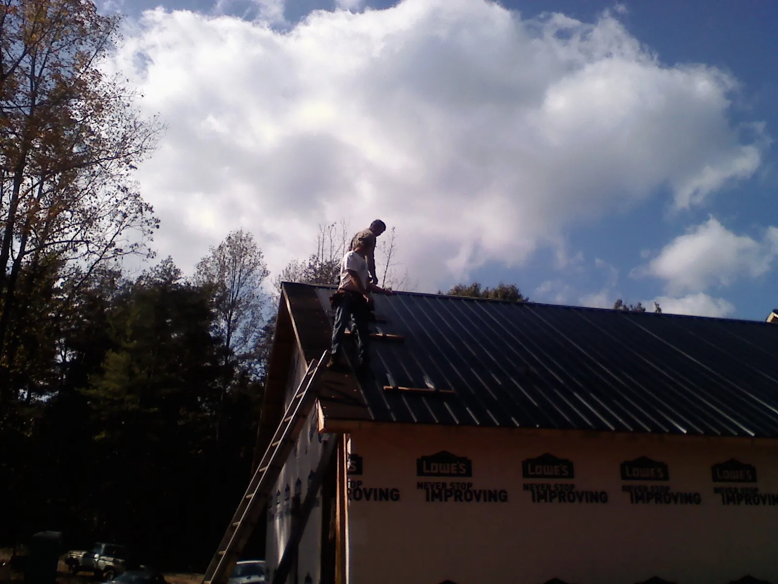 Roofer fastening dark metal panels high against a cloudy sky, from a Roof Inspection job in Wilson Creek