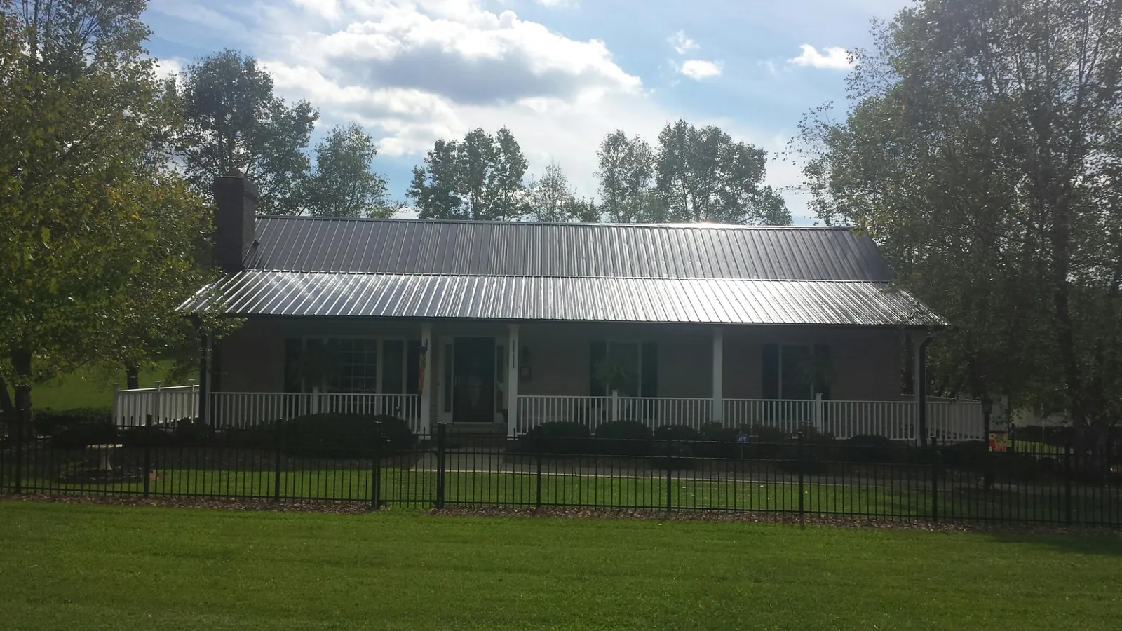 Gray metal roof on a brick ranch with a full width front porch — Gutter Guard Installation work by our crew in Wilson Creek