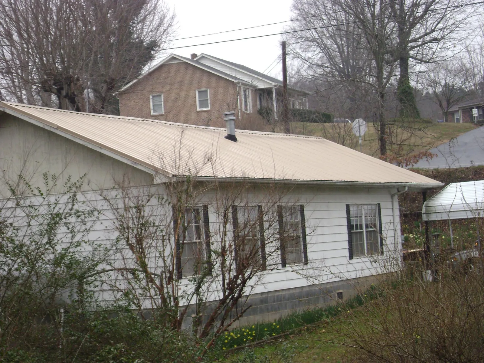 Tan metal roof on a white sided house set into a hillside — Commercial Roofing by Roofing Brothers in Wilson Creek