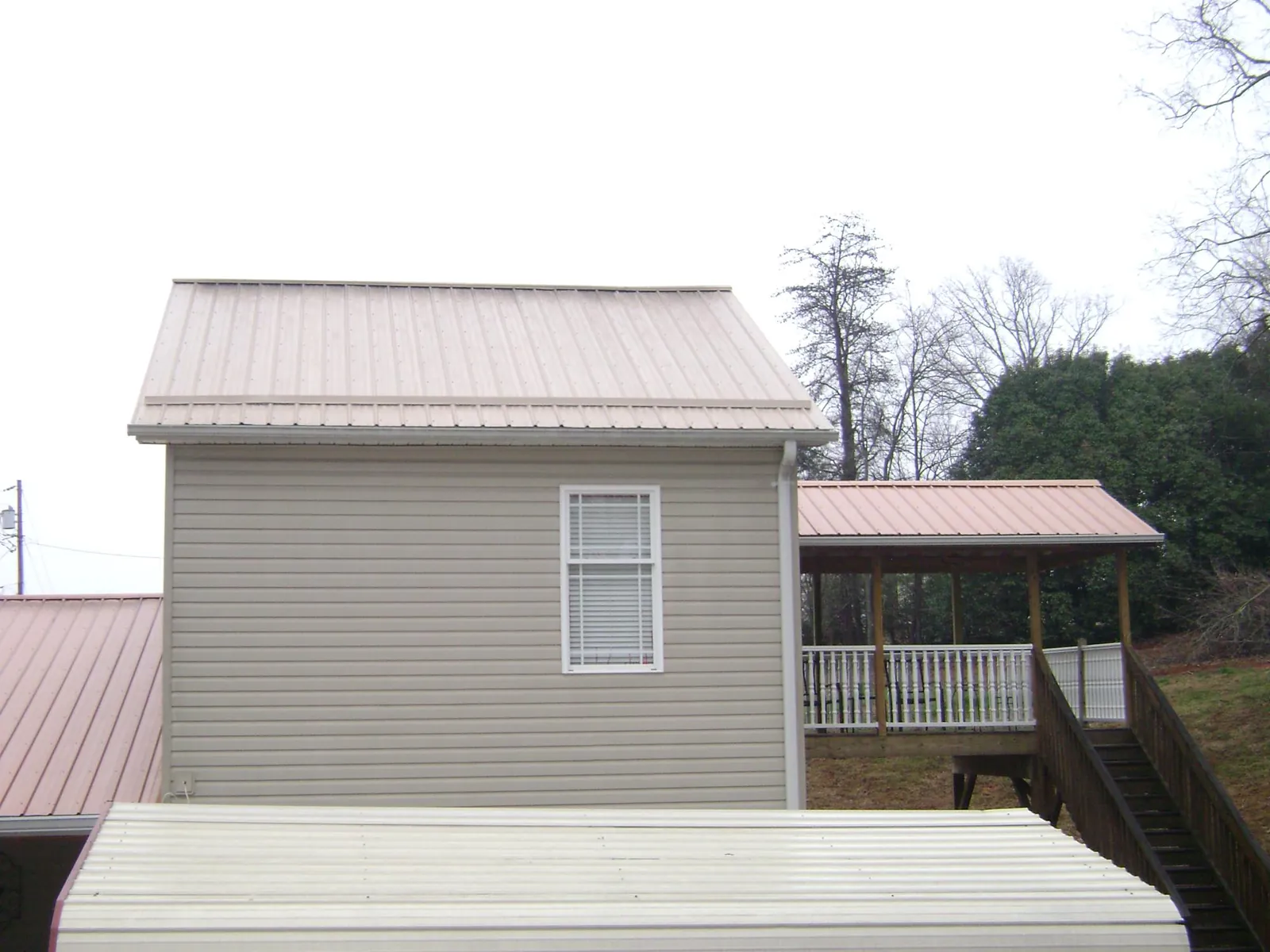Tan metal roofs on a two story addition and attached porch, from a Roof Replacement job in Wilson Creek